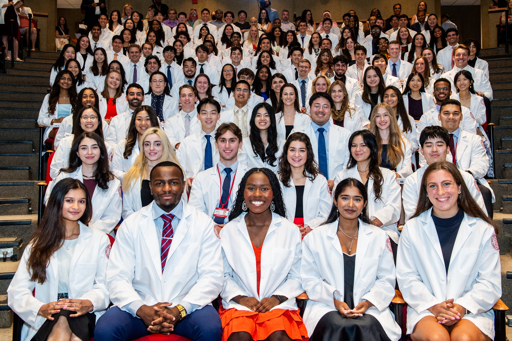 Wide shot of students seated in audience wearing white coats 
