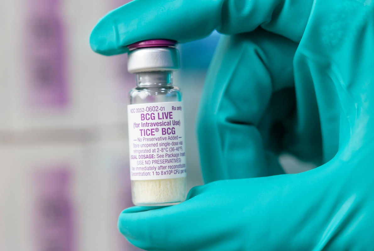 Green-gloved hand holding vial of BCG