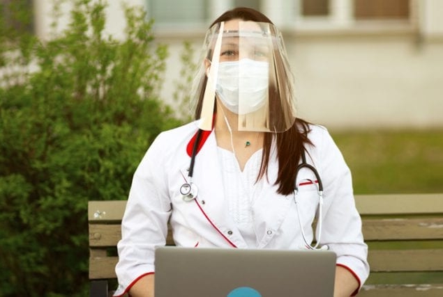 Medical professional, wearing a mask and face shield, sitting on a bench outside