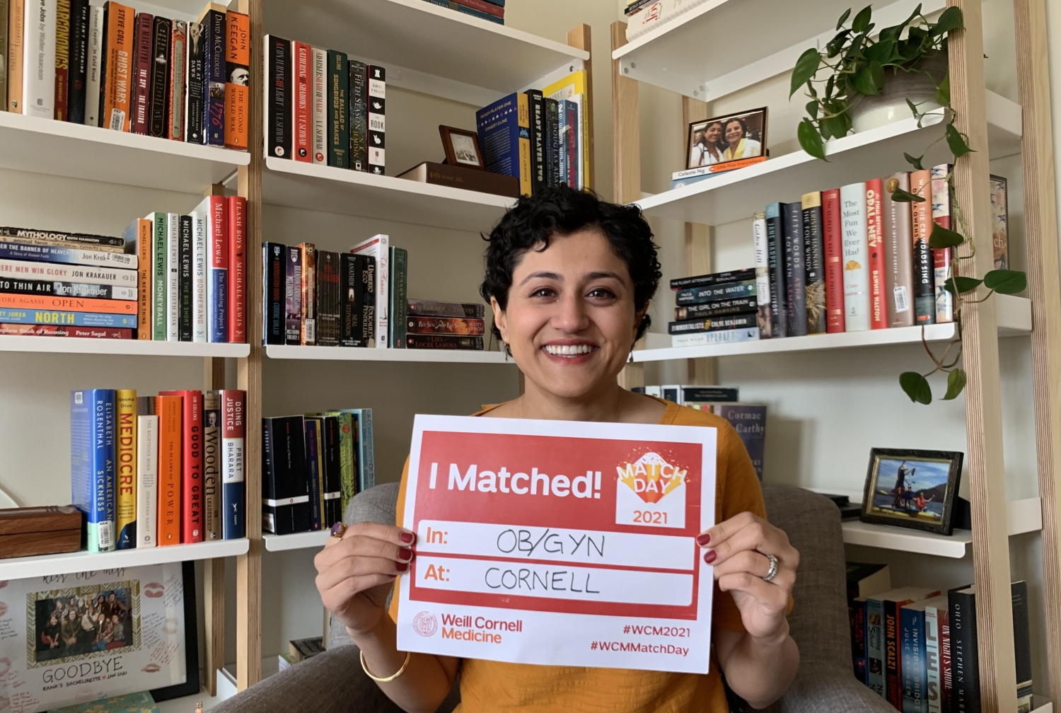 a woman smiling for a photo, holding a sign showing where she matched for Match Day 2021