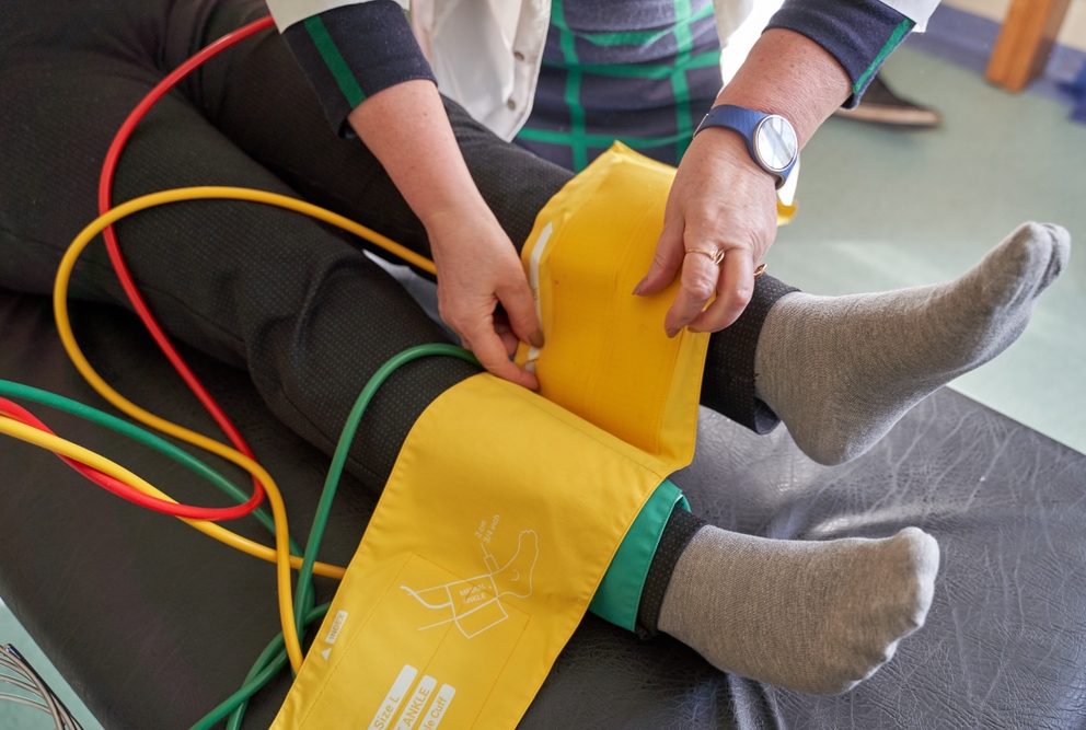 photo of person wrapping blood pressure cuff around lower leg of patient