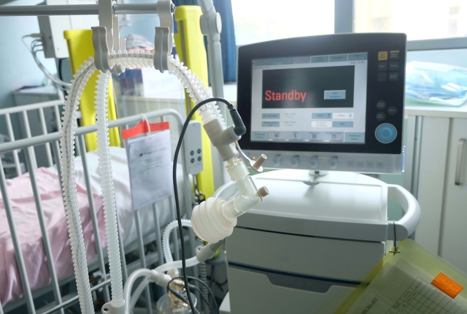 ventilator monitor reading 'standby' in foreground with hospital bed in background