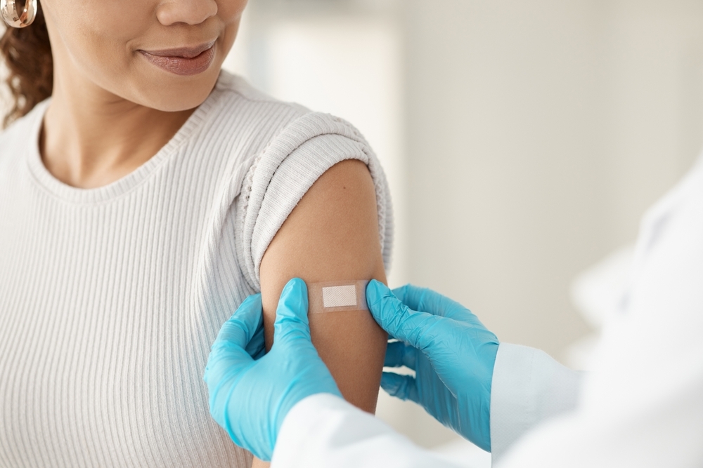 person with gloves placing an band-aid on a woman's upper arm