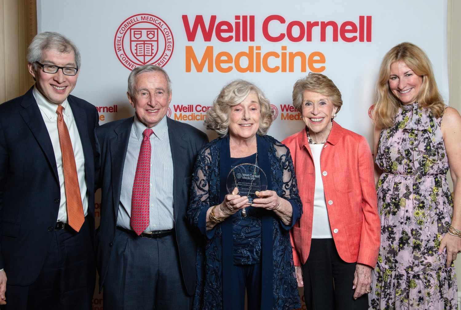 Five people pose for a group shot behind a Weill Cornell Medicine backdrop