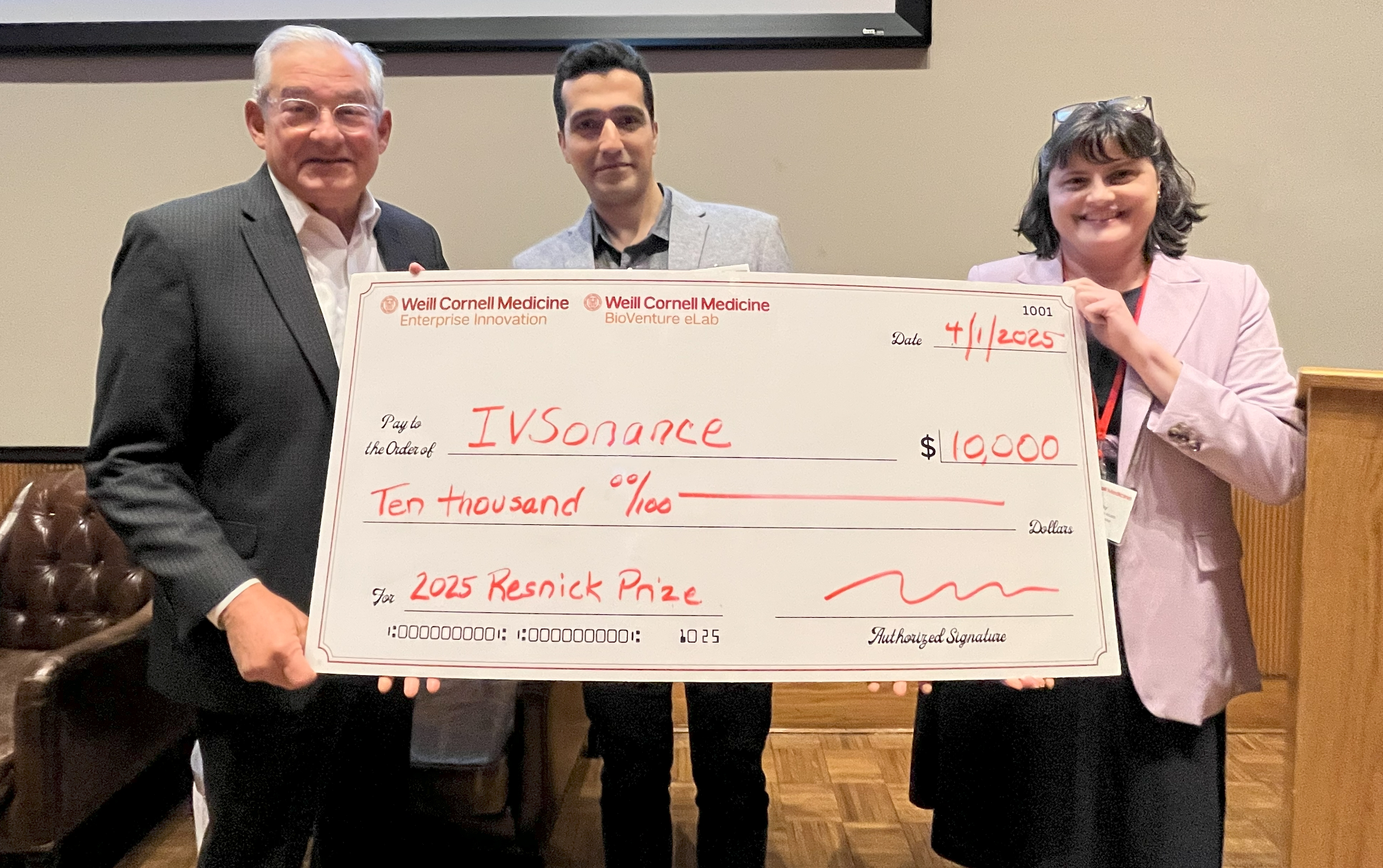 A group of three people in business attire (from left: an older man, a young man and a middle-aged woman) holding a big check of $10,000.