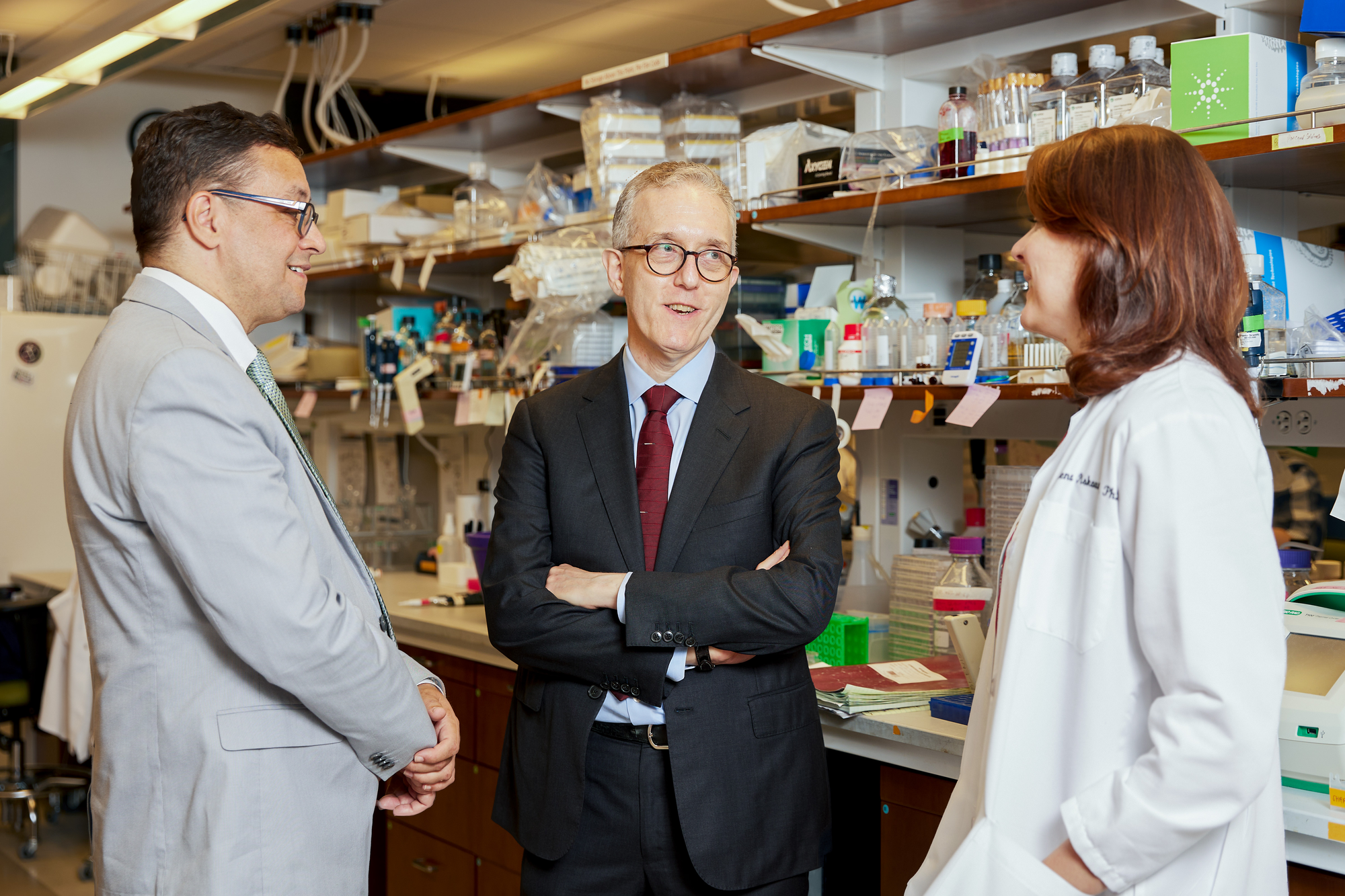 Two men in suits and a woman in white coat talking in a lab