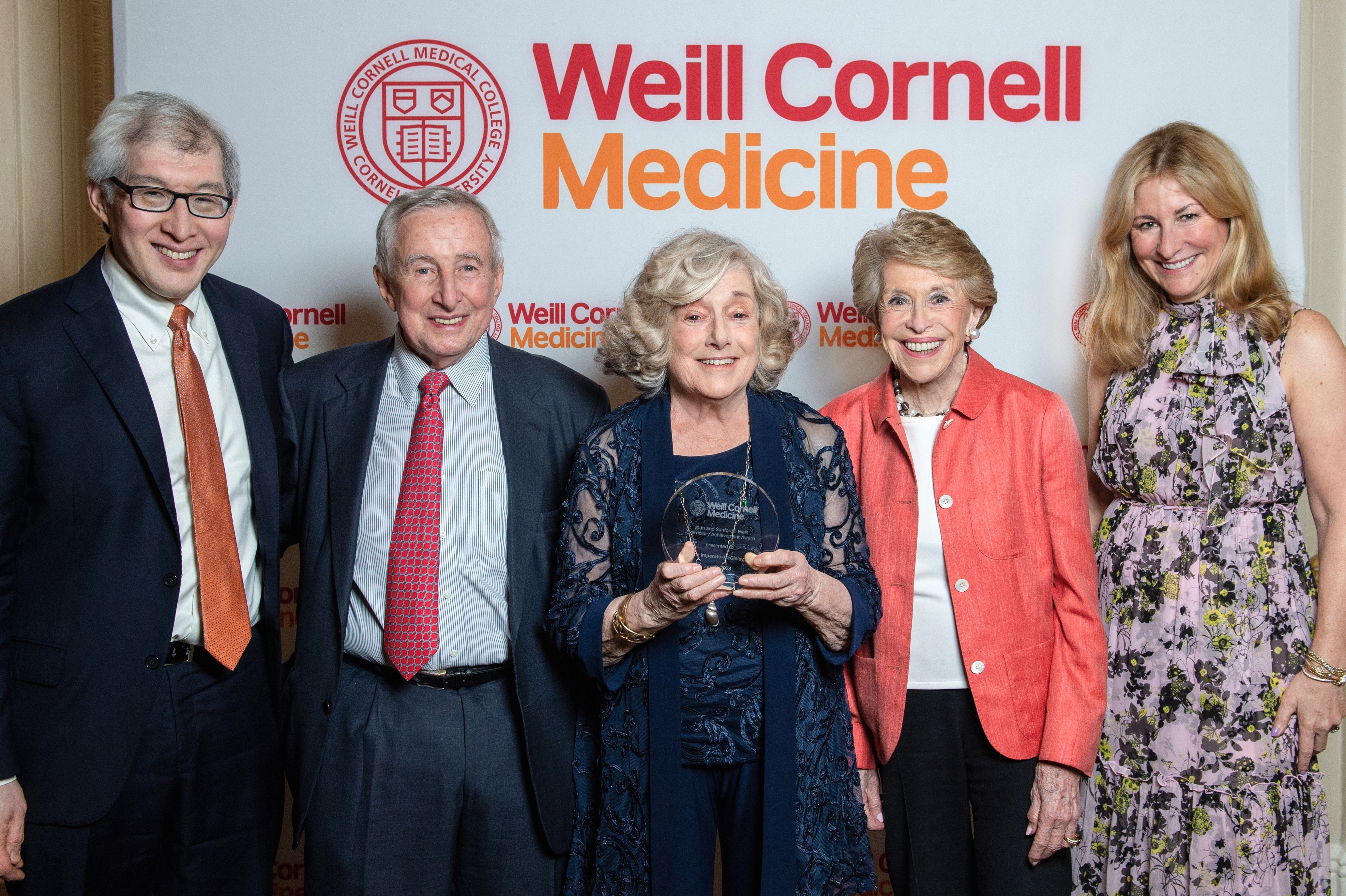 Five people pose for a group shot behind a Weill Cornell Medicine backdrop