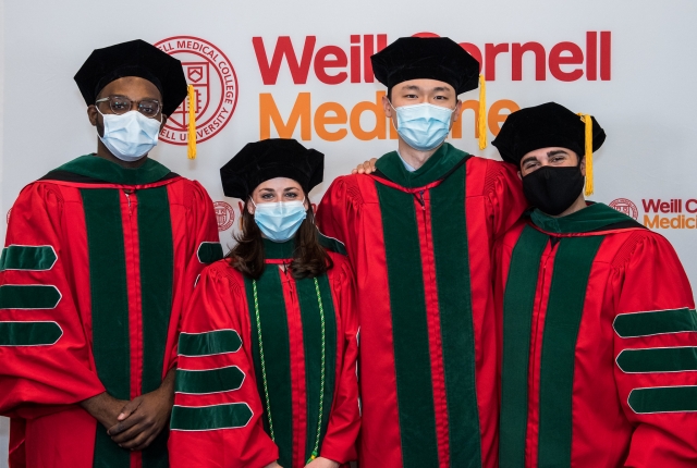 Masked graduating students standing in front of a WCM backdrop